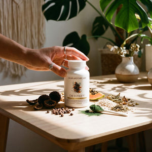 Hand reaching for the Detoxify bottle in a sunlit room with botanicals